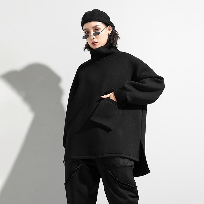 Woman wearing black oversized turtleneck pullover with utility pocket details.