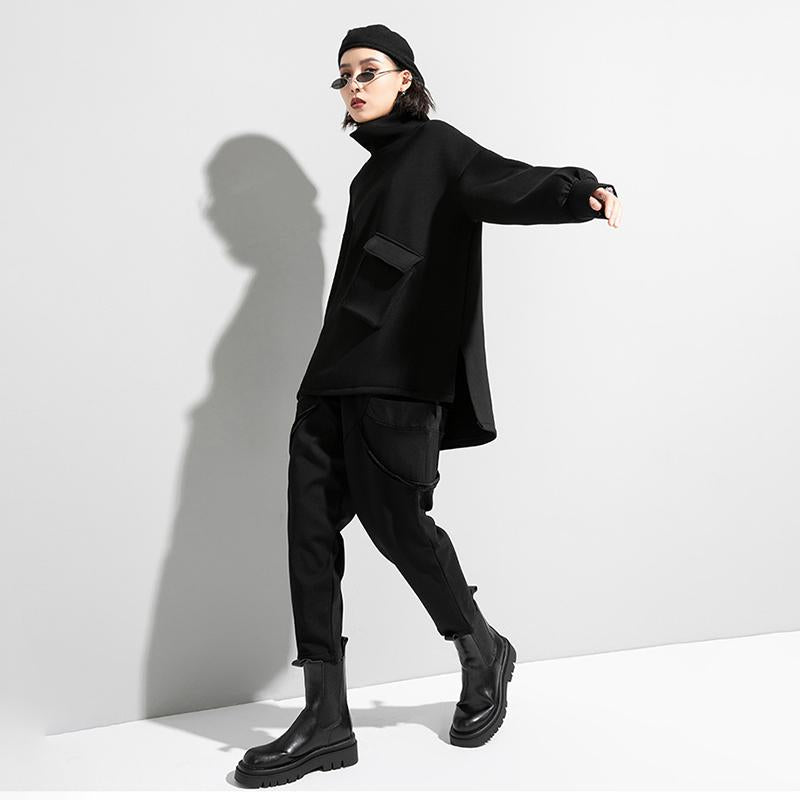 Woman wearing black oversized turtleneck pullover with utility pocket details.