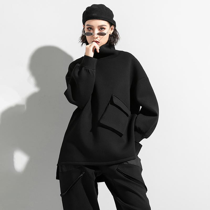 Woman wearing black oversized turtleneck pullover with utility pocket details.