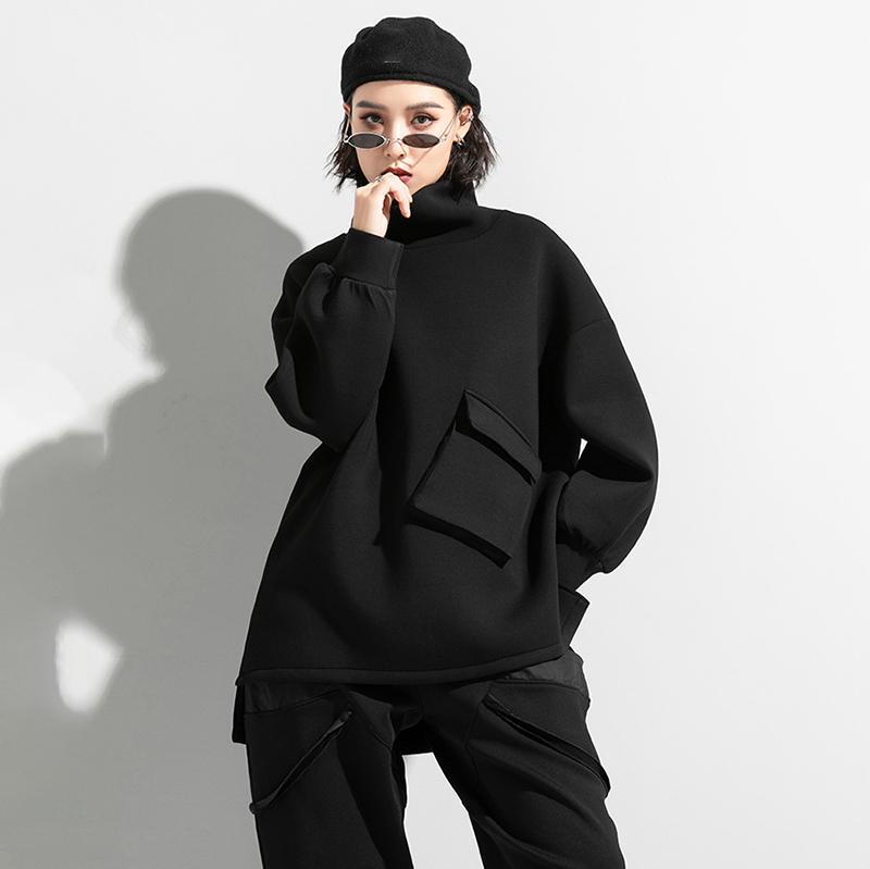 Woman wearing black oversized turtleneck pullover with utility pocket details.