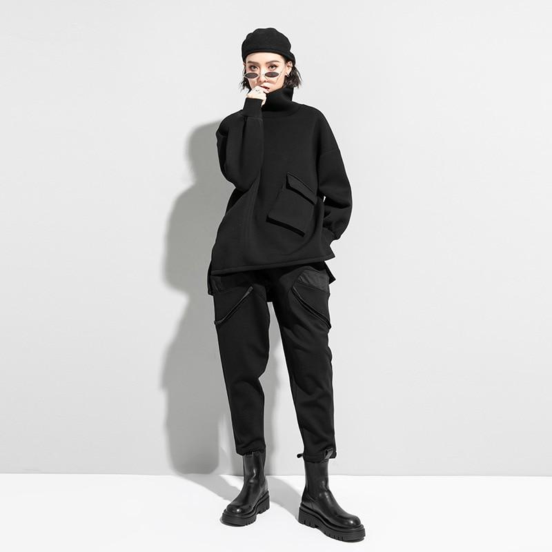 Woman wearing black oversized turtleneck pullover with utility pocket details.