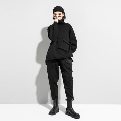 Woman wearing black oversized turtleneck pullover with utility pocket details.